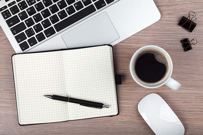 Ordenador, libreta con boli, café y ratón sobre mesa de madera. Razones por las que nadie lee tu blog